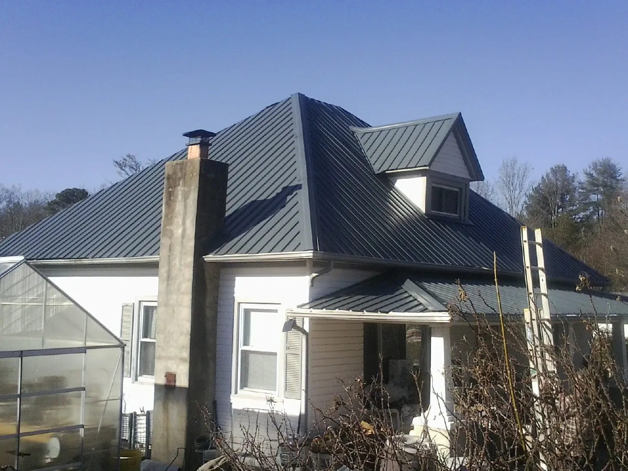 Dark blue standing seam metal roof on a white farmhouse with dormer — Slate & Tile Roof Repair by Roofing Brothers in East Fultonham