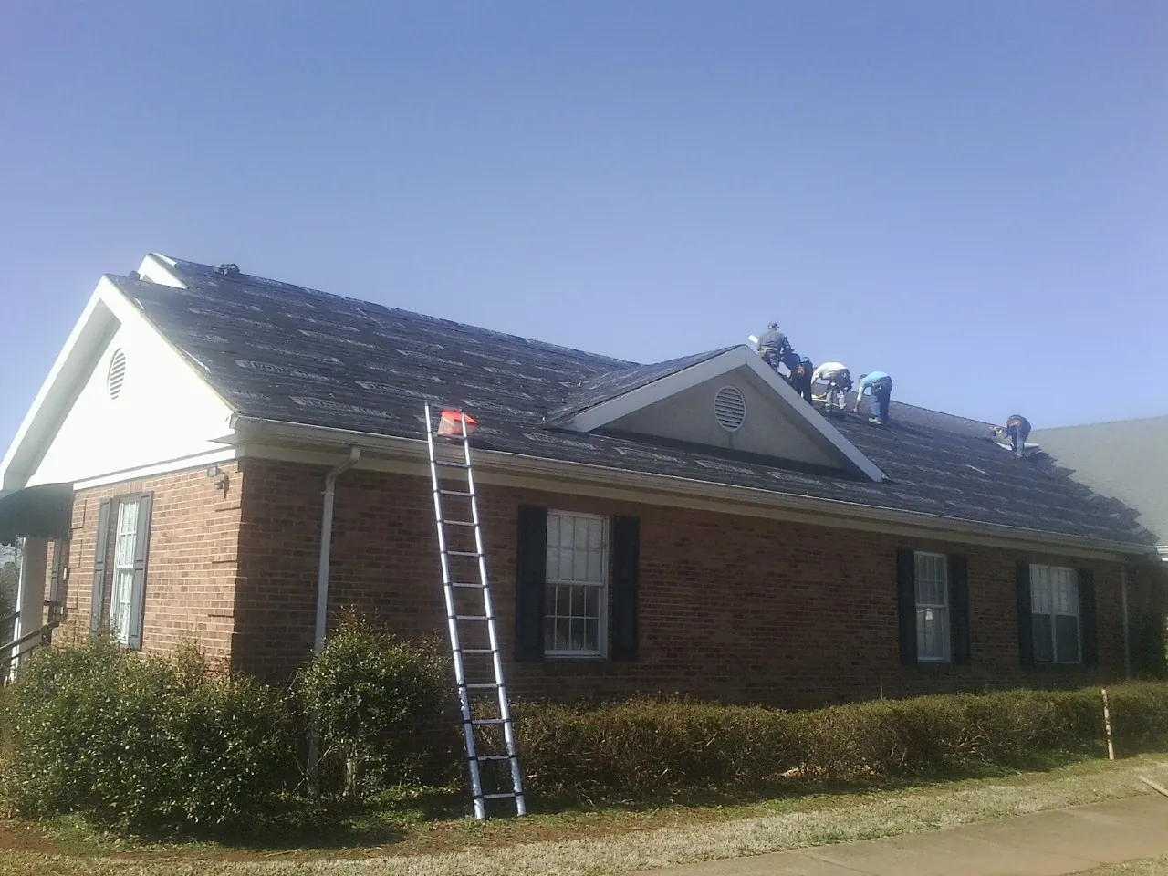 Crew tearing shingles off a brick ranch roof with a ladder set — Metal Roof Repair work by our crew in East Fultonham