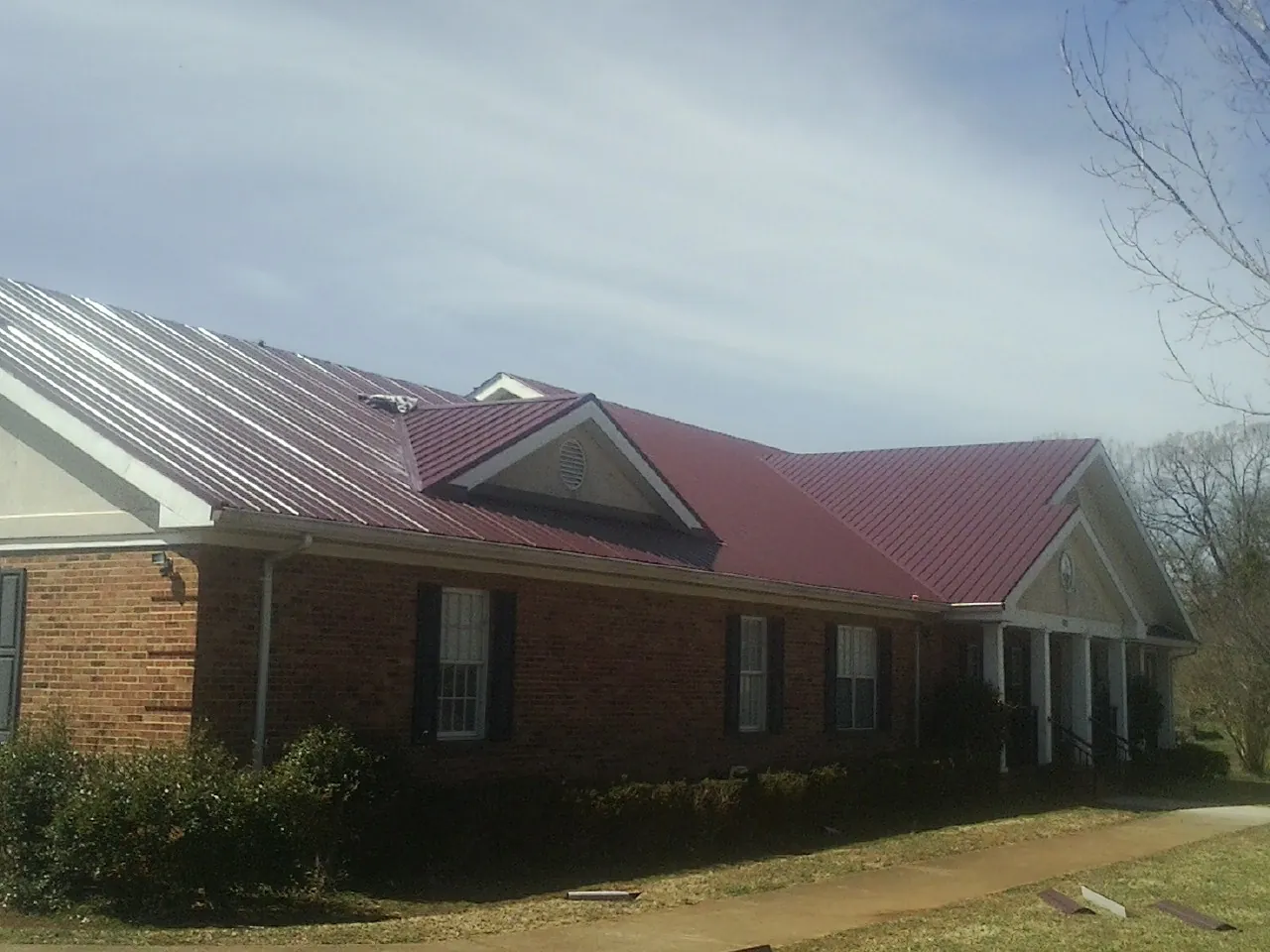 Red metal roof with gabled entries on a long brick building, from a Hail Damage Roof Repair job in East Fultonham