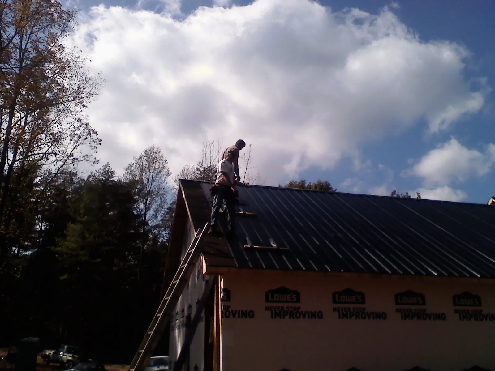 Roofer fastening dark metal panels high against a cloudy sky, from a Roof Inspection job in East Fultonham