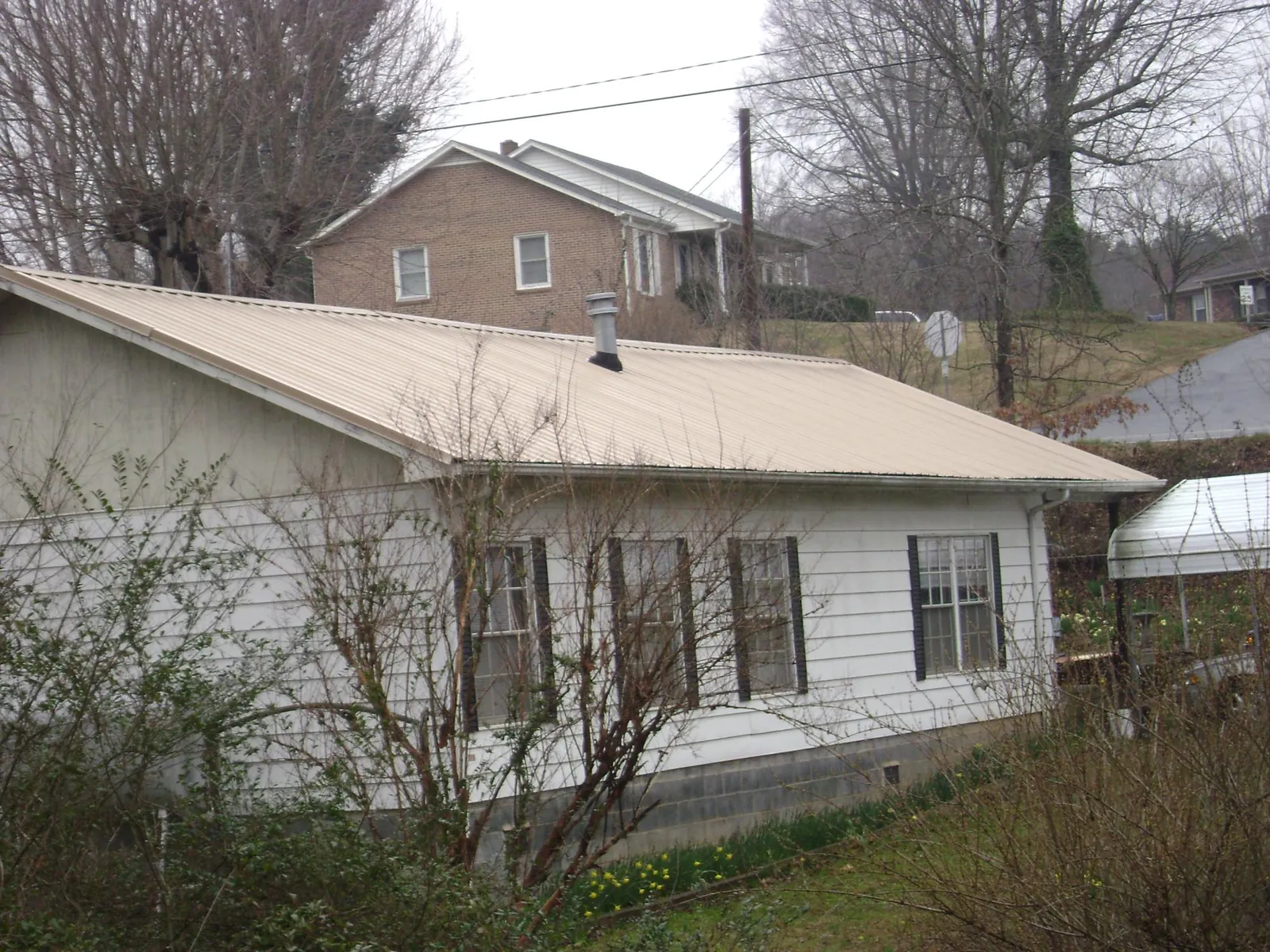 Tan metal roof on a white sided house set into a hillside — Commercial Roofing by Roofing Brothers in East Fultonham